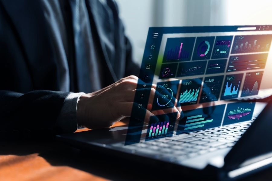 Close-up of a businessman typing on a laptop with a transparent digital dashboard overlay.