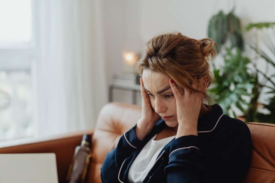 A stressed woman holding her head while sitting on a couch, highlighting the need for boundary-setting strategies.