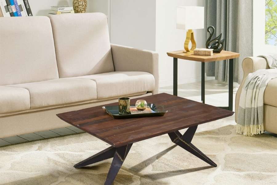 A dark wooden coffee table with geometric metal legs stands in a bright living room in front of a beige sofa.